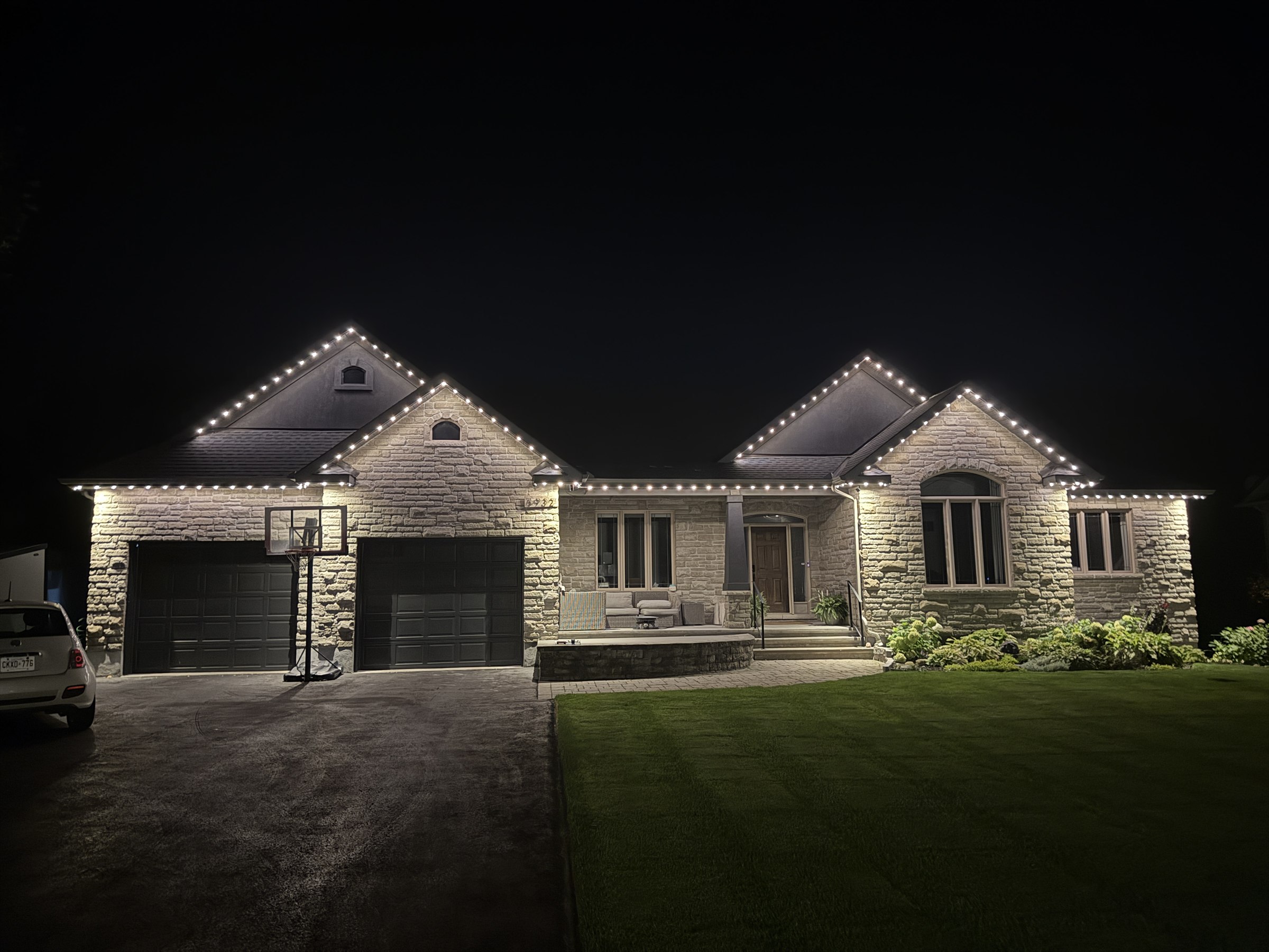 Warm white permanent outdoor lighting following the rooflines and centred peaks of a stone home in Ottawa