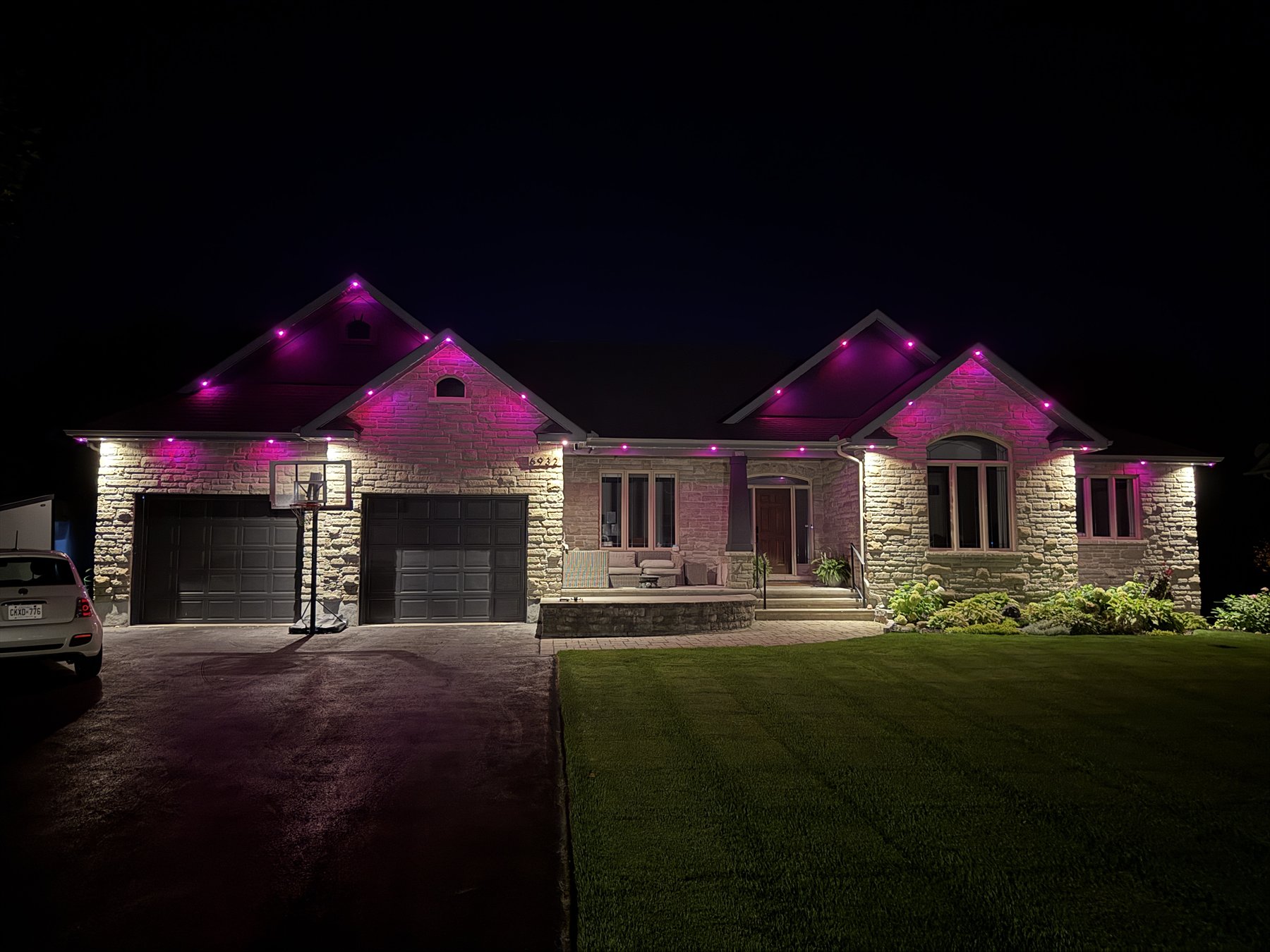 Magenta permanent roofline lighting washing the peaks of a stone bungalow
