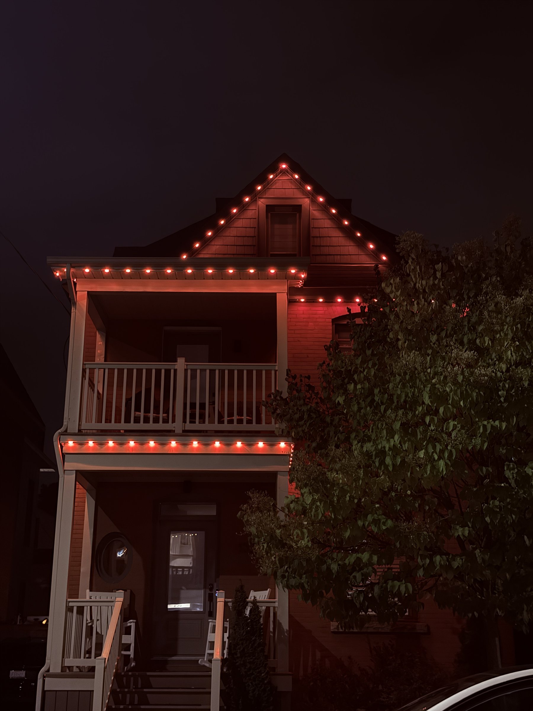 Red permanent lighting following the roofline and balconies of an urban home