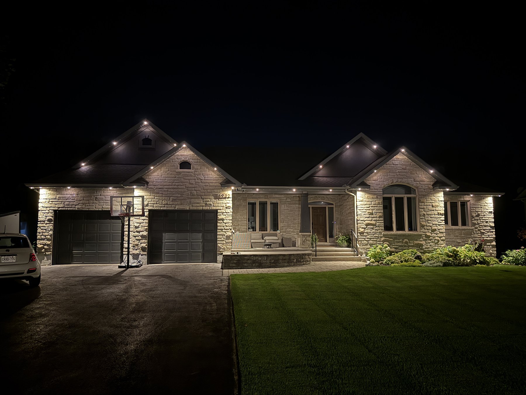 Soft warm-white permanent lights highlighting the peaks of a stone bungalow